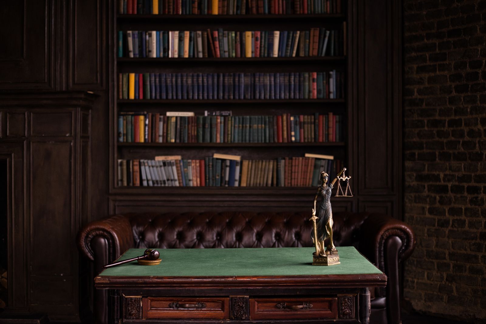 Law study with bookshelves, a gavel, and a Lady Justice figurine on a green felt desk